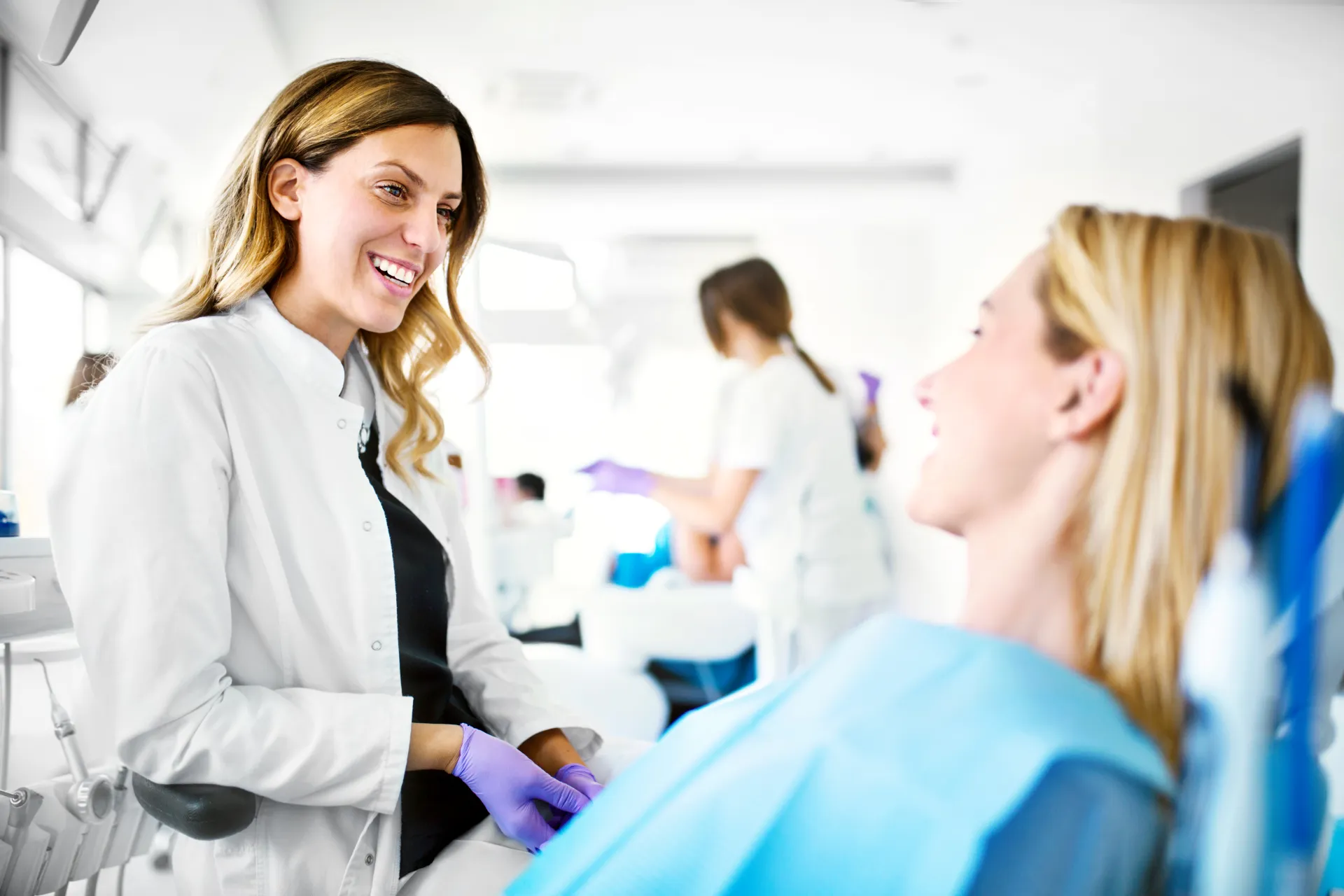 A dentist in a white coat smiling with a patient seated in the treatment chair